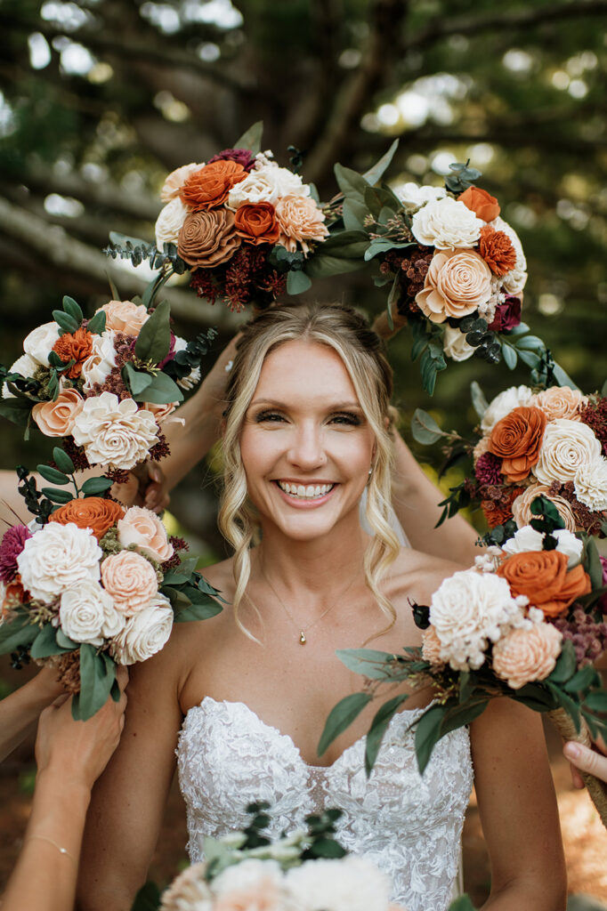 Bride smiling while bridesmaids hold bouquets around her during wedding portraits at The Lodge at Rush Lakes.