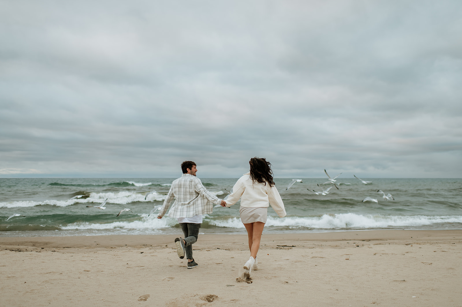 Couple running towards the beach for their winter engagement photos in New Buffalo, MI.