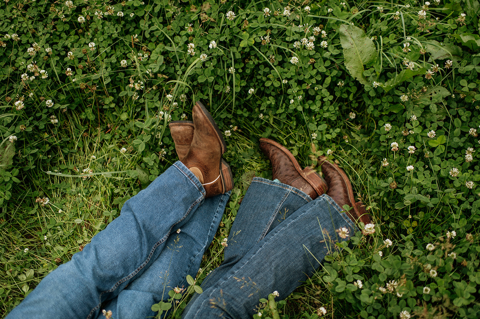 Close up shot of a couple wearing boots while laying in the grass.