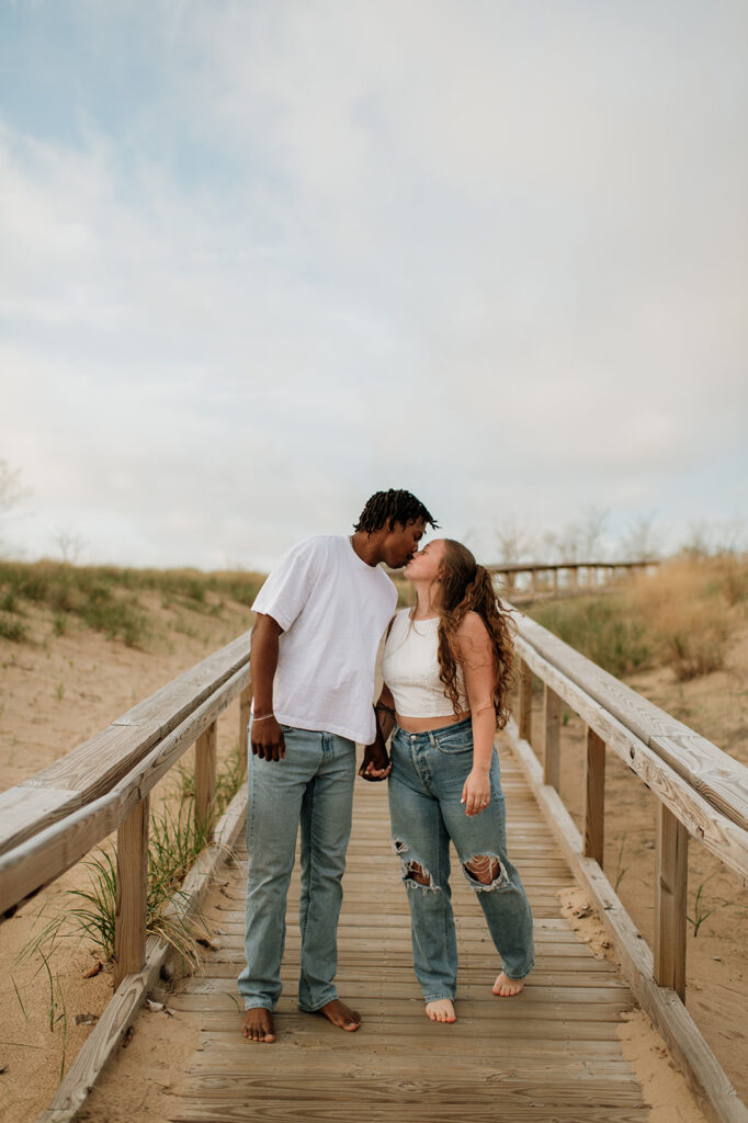 Couple kissing on a wooden path during their New Buffalo Beach engagement photos.