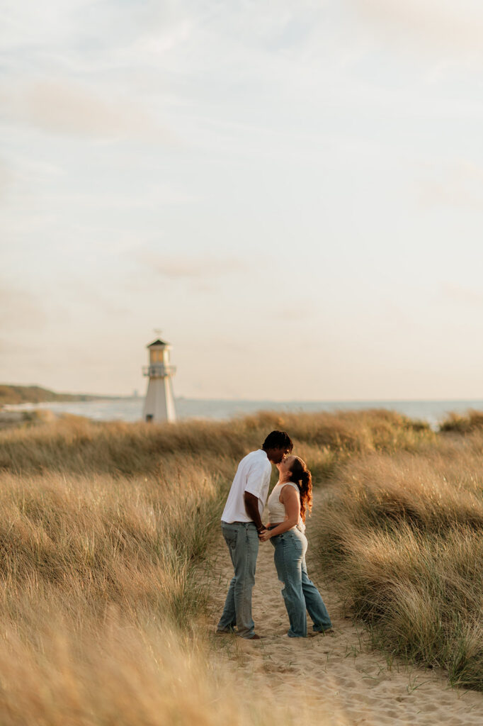 Couple kissing with the lighthouse in the back during their New Buffalo Beach engagement photos.