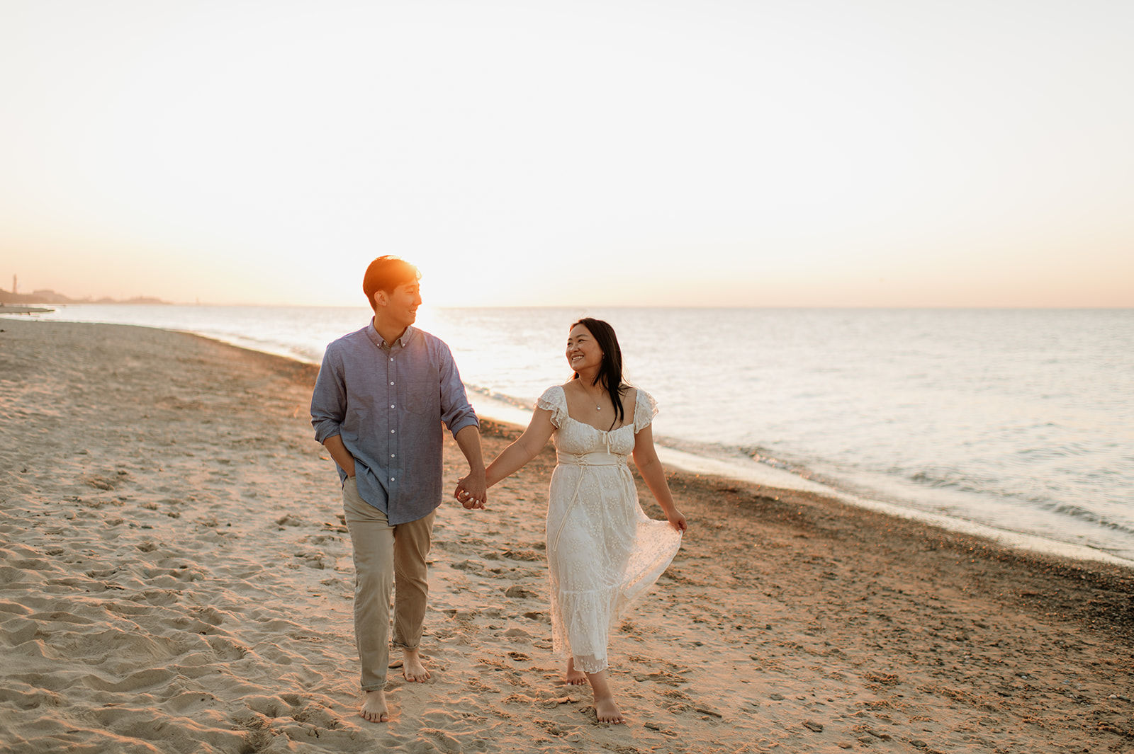 Couple holding hands and walking along the beach at sunset.