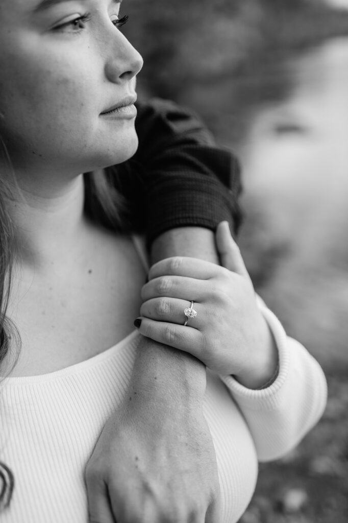 Black and white engagement detail shot of a man with his arm wrapped around his fiancé while showing off her engagement ring.