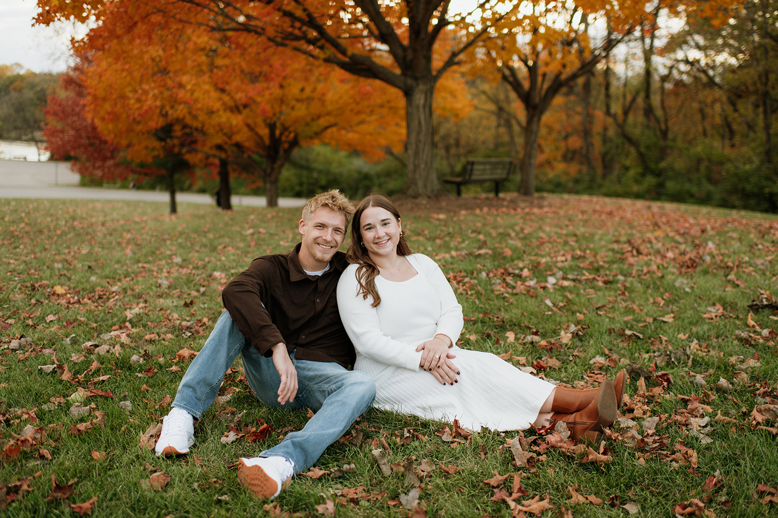 Couple smiling at the camera while they sit in the grass.
