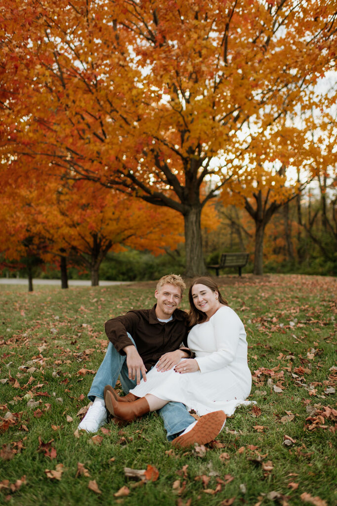 Couple sitting together in the grass during their fall engagement.