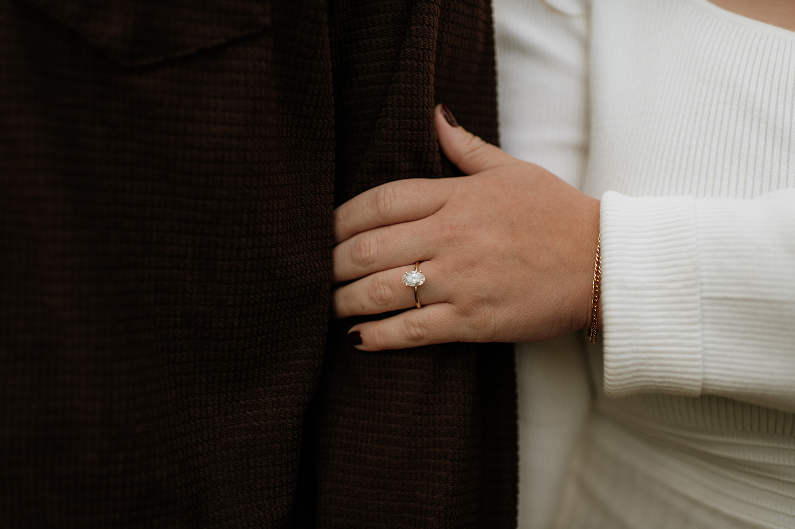 Close up shot of a bride to be holding her fiancés arm and showing off her engagement ring.