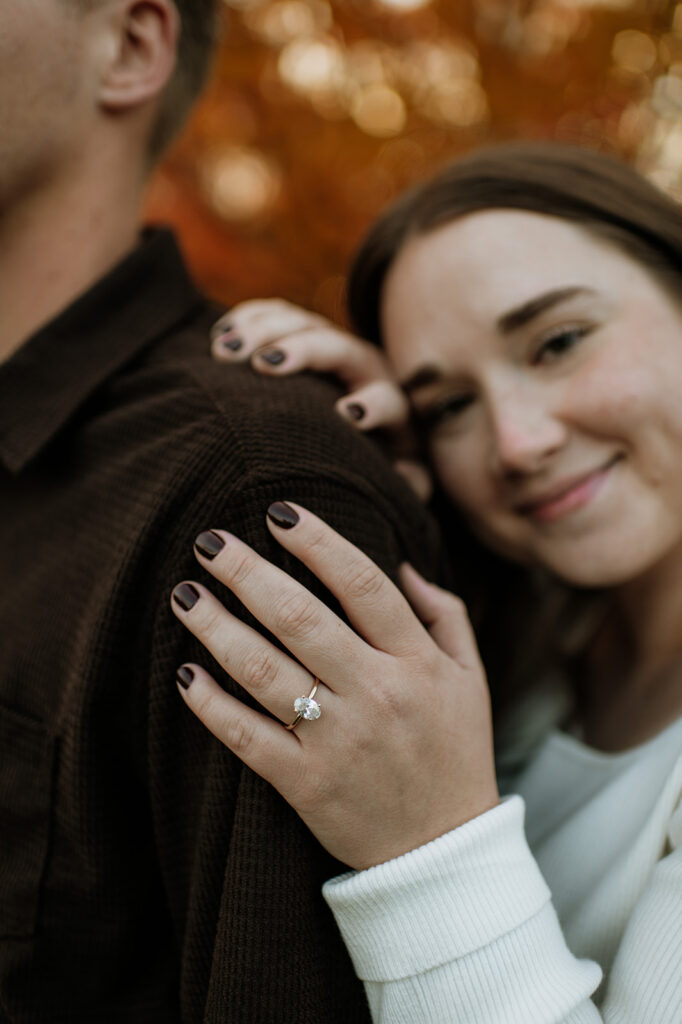 Woman resting her hand on her fiancés shoulder and showing off her engagement ring.