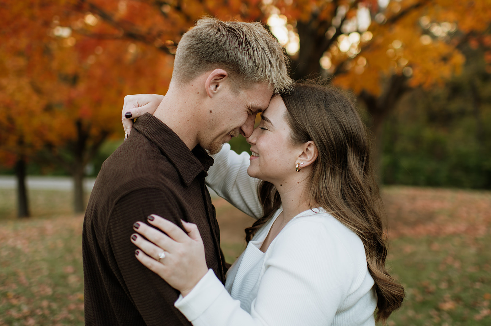 Couple touching noses with fall foliage in the backdrop.
