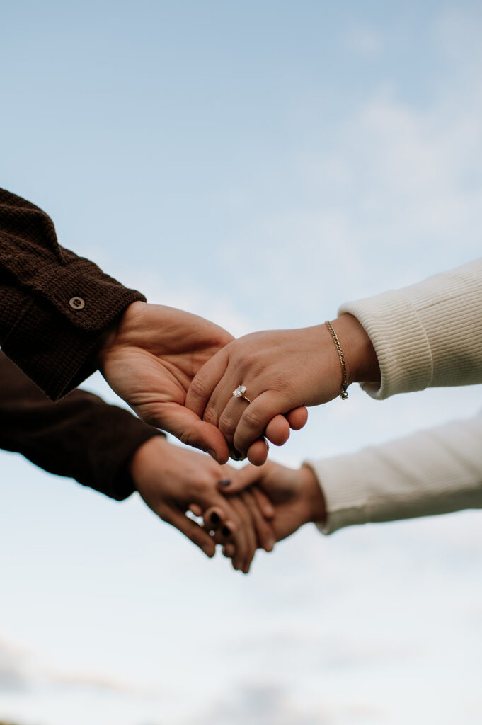 Photo of a couple holding hands with the sky above showing of an engagement ring.