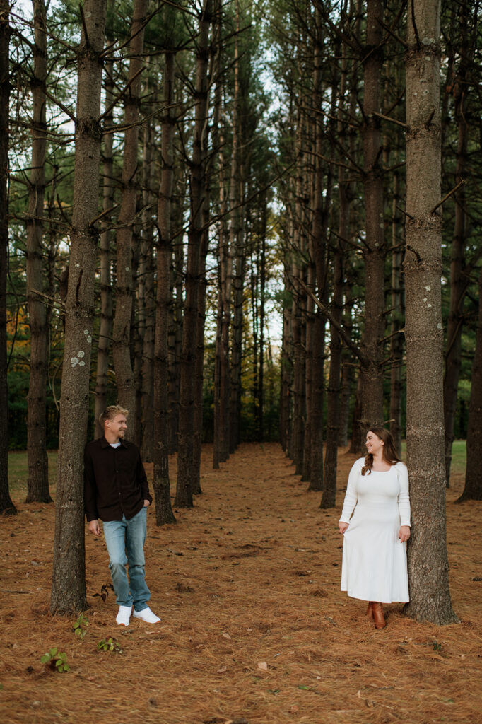 Couple leaning against trees across from one another during their South Bend engagement photos at St. Patrick’s County Park.