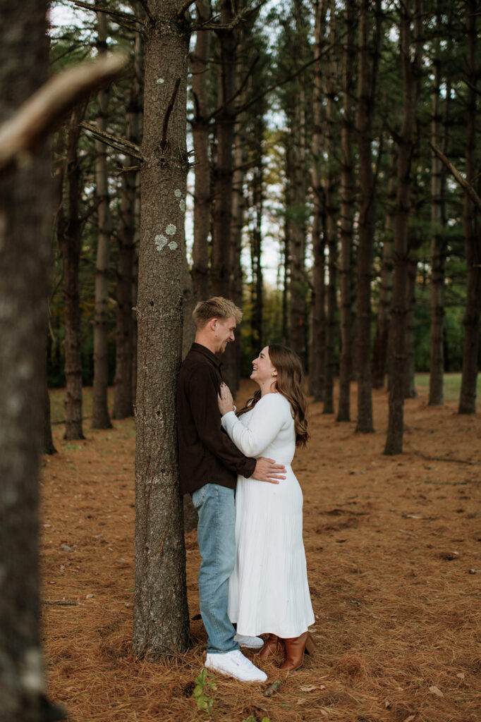 Couple posing amongst tall trees for their fall engagement.