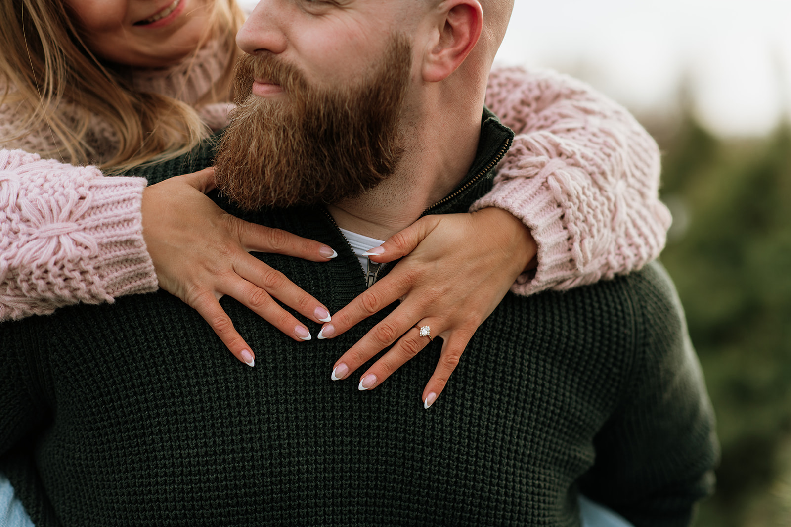 Woman holding her fiancés shoulders from behind and showing off her engagement ring.