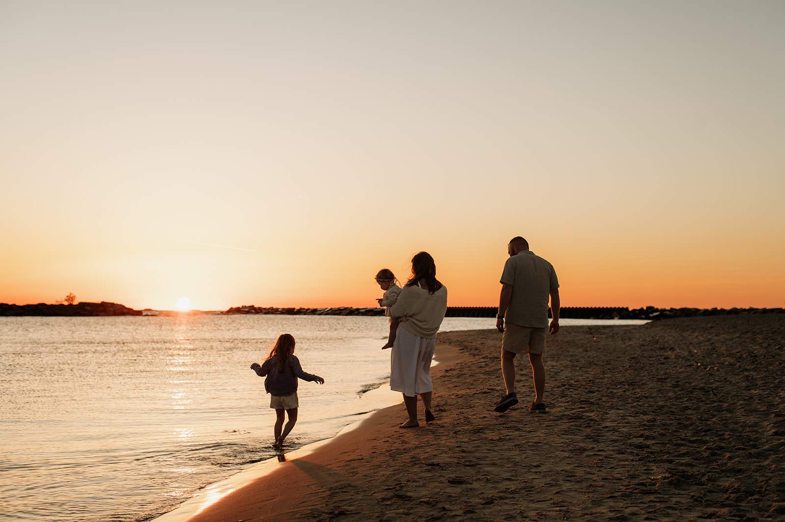 Family of four walking the shoreline at New Buffalo beach at sunset.