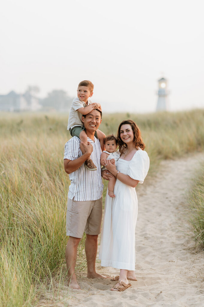 Family of four posing at New Buffalo Beach with the lighthouse in the background.