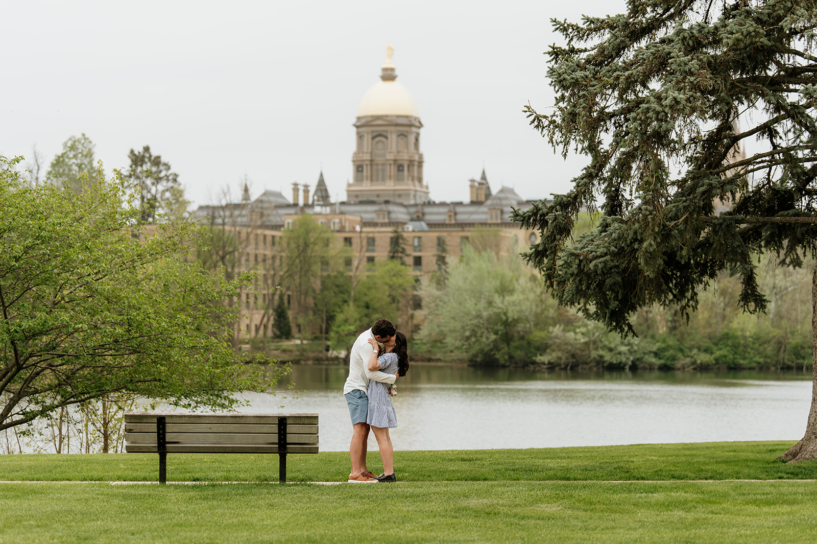Wide shot of a couple kissing after their Notre Dame proposal in front of Saint Joseph's Lake.