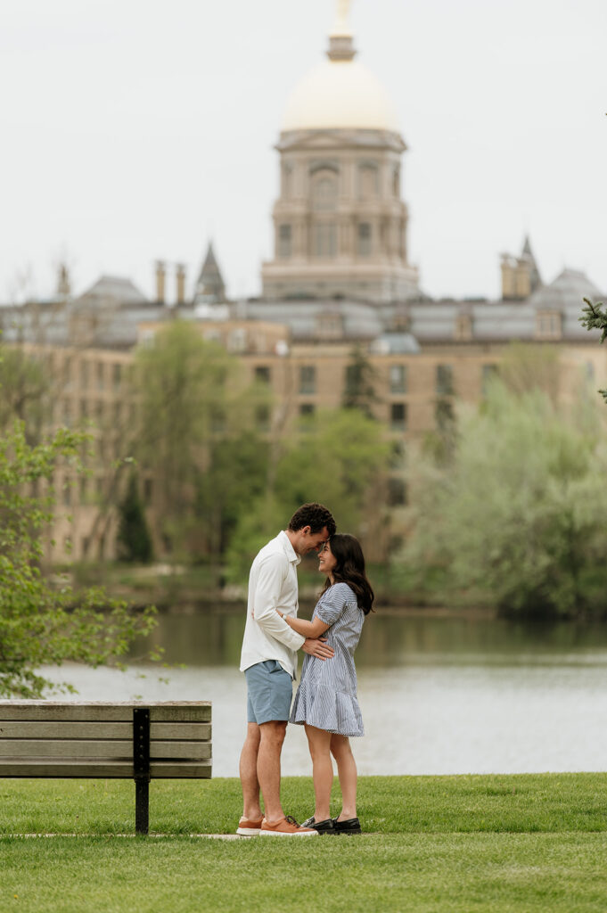 Man and woman standing forehead to forehead in front of Saint Joseph's Lake and the Golden Dome at The University of Notre Dame.