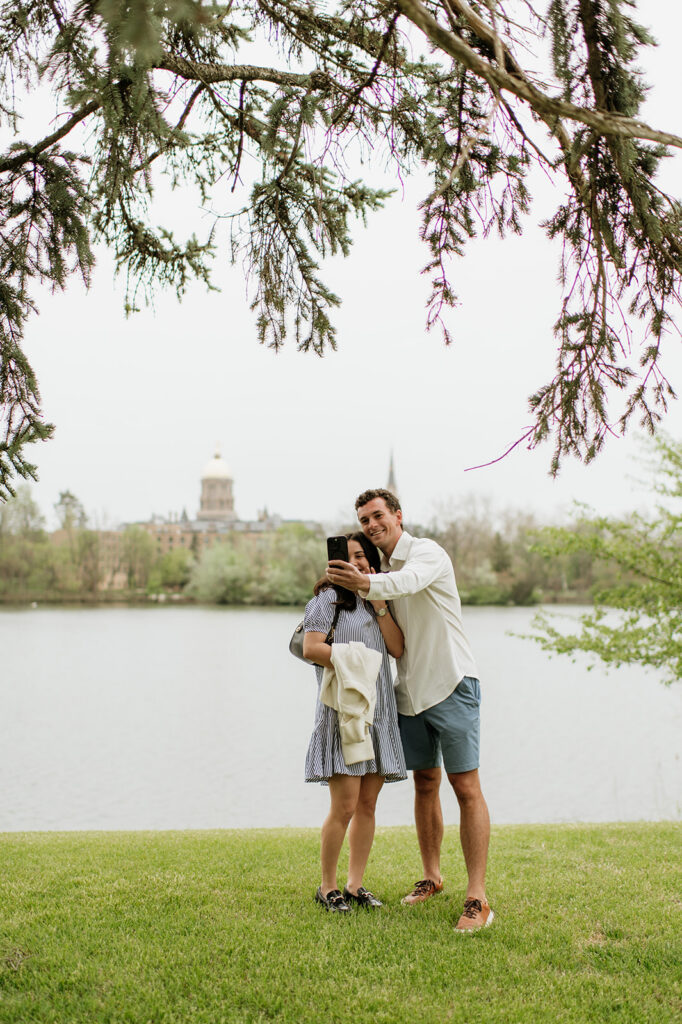 Man and woman taking a selfie in front of Saint Joseph’s Lake at The University of Notre Dame.