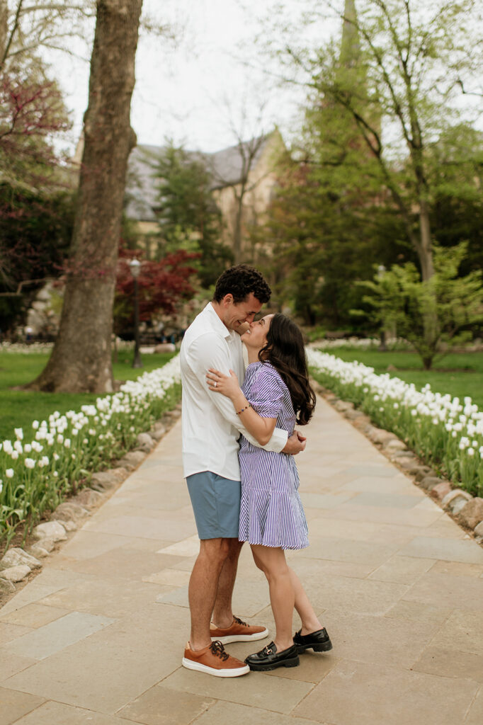 Couple touching noses on a pathway surrounded by white tulips after their Notre Dame proposal.