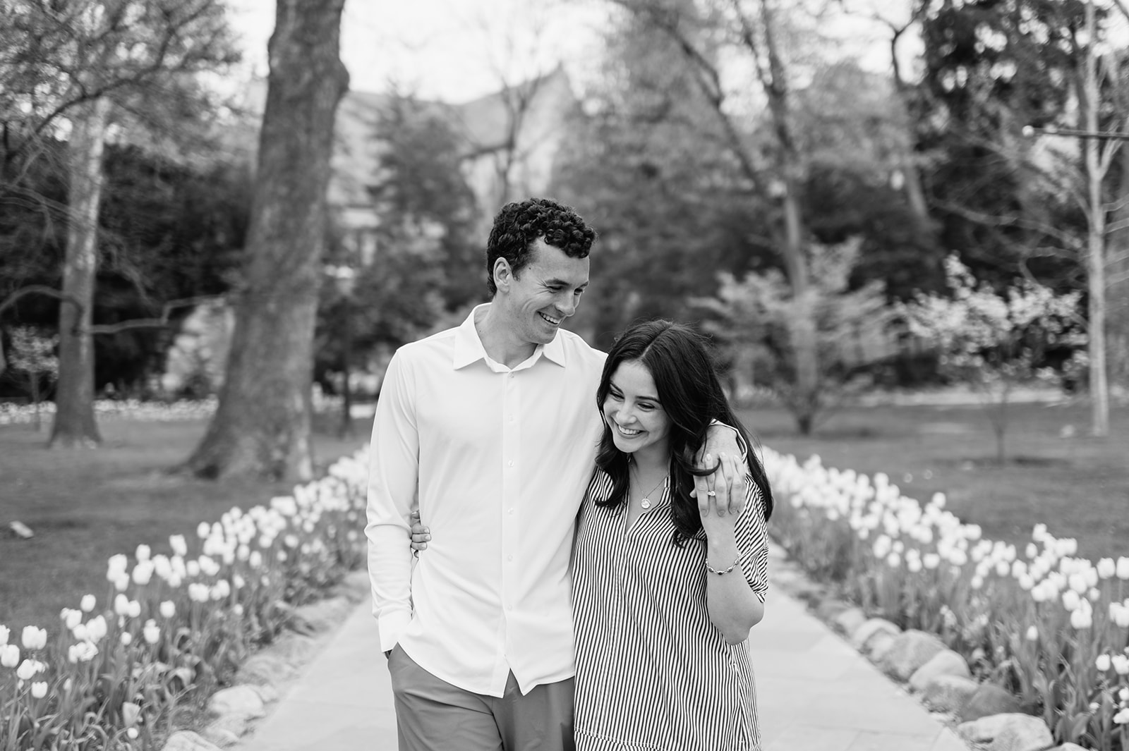 Black and white photo of a couple walking a floral lined pathway at University of Notre Dame for their engagement photos.