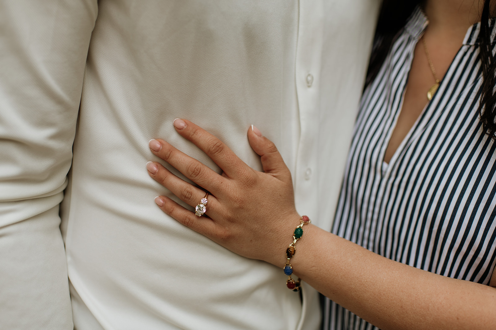 Close up wide shot of a woman resting her hand on her fiancés chest while showing off her engagement ring.