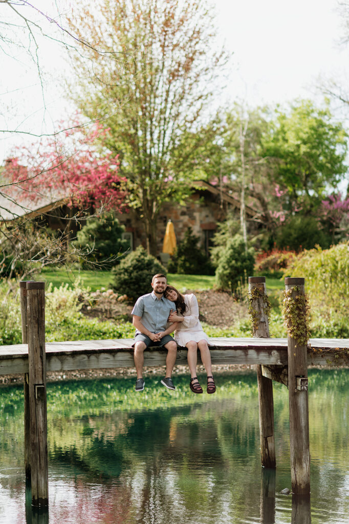 Couple sitting on a dock in Gamstra Gardens for their Northern Indiana engagement photos.