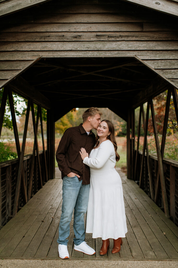 Man kissing his fiancés forehead as they post under a wooden structure at St. Pats in South Bend - a Northern Indiana Photo Location.