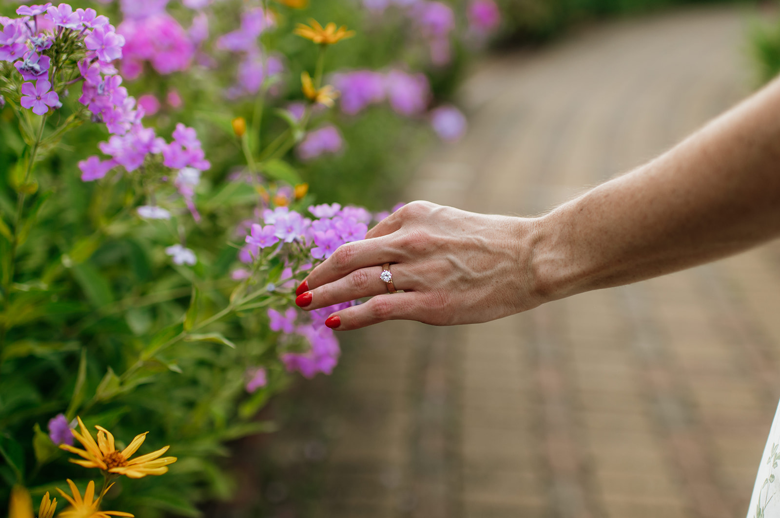 Woman's hands touching flowers inside of a garden showing off her engagement ring.