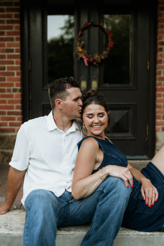 Man kissing the side of his fiancés head as they pose for photos.
