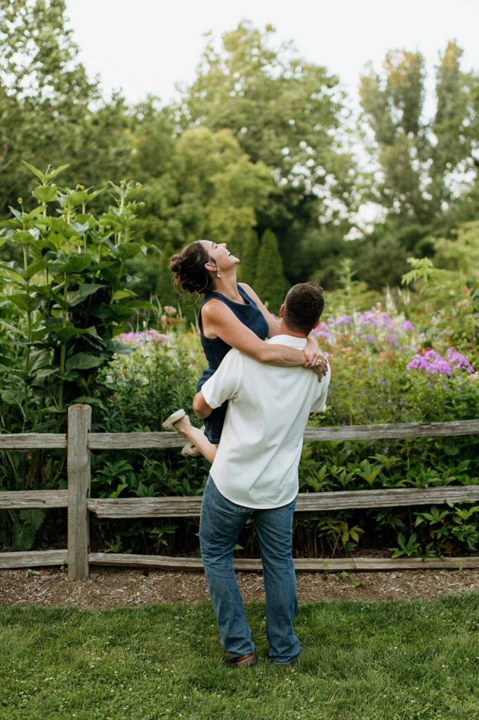Man lifting up his fiancé during their engagement photos at Defries Gardens in New Paris, Indiana.