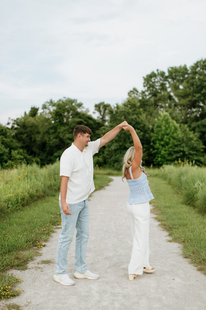 Man twirling his fiancé on a trail during their Cobus Creek County Park Engagement Photos in Elkhart, Indiana.