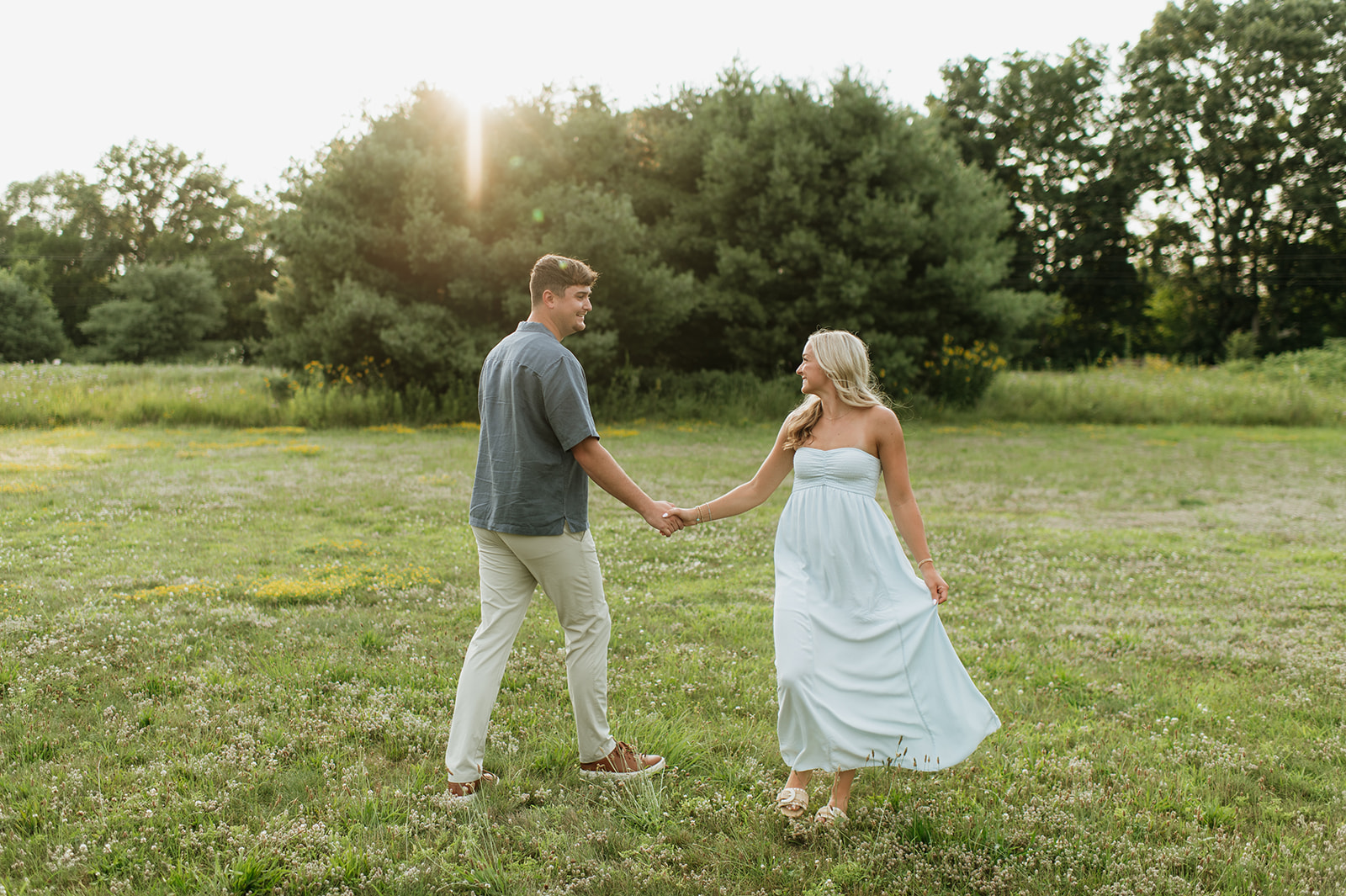 Couple walking hand in hand in a field during golden hour.