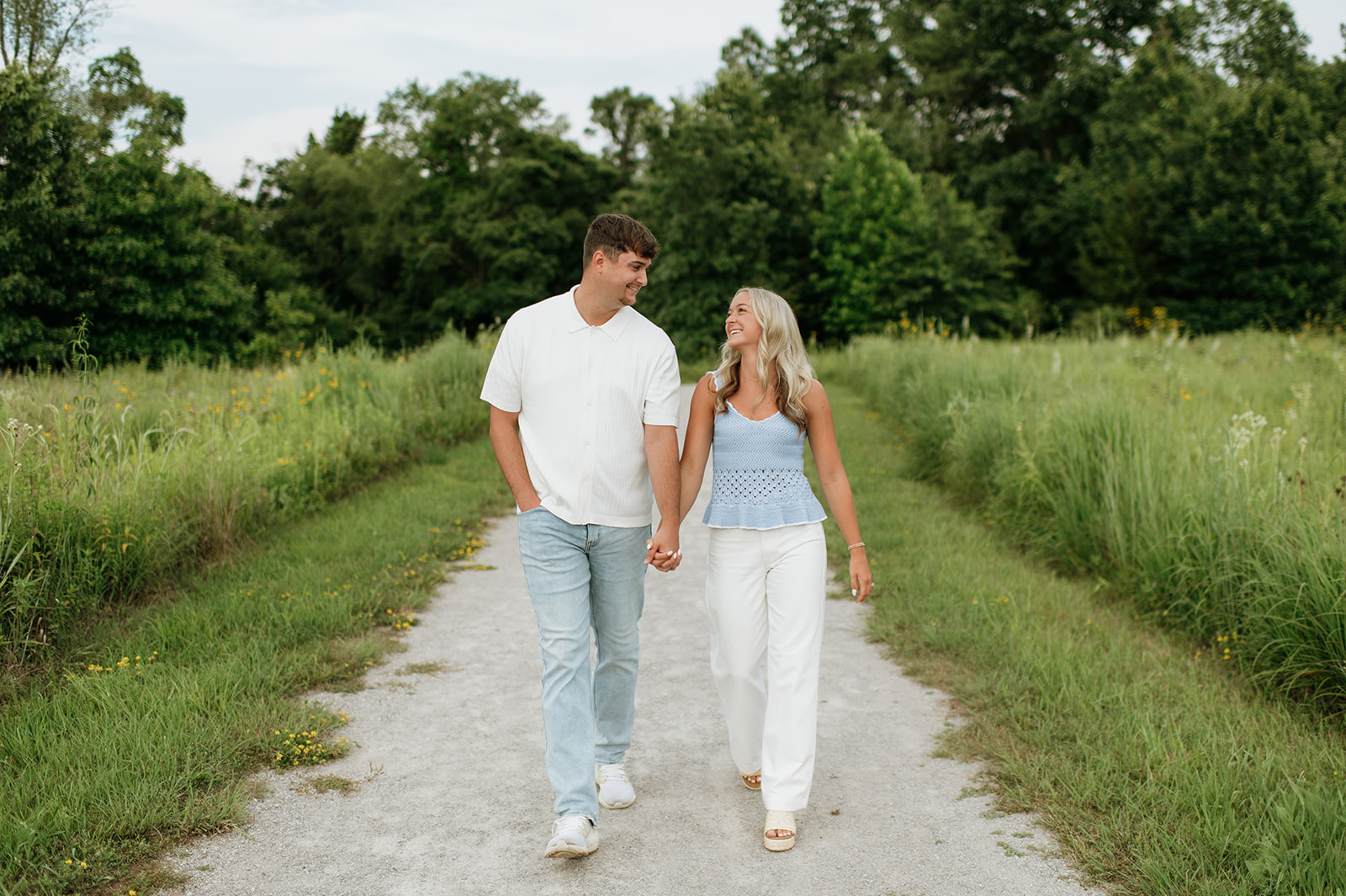 Couple walking hand in hand down a trail for their Cobus Creek County Park engagement photos near South Bend, Indiana.