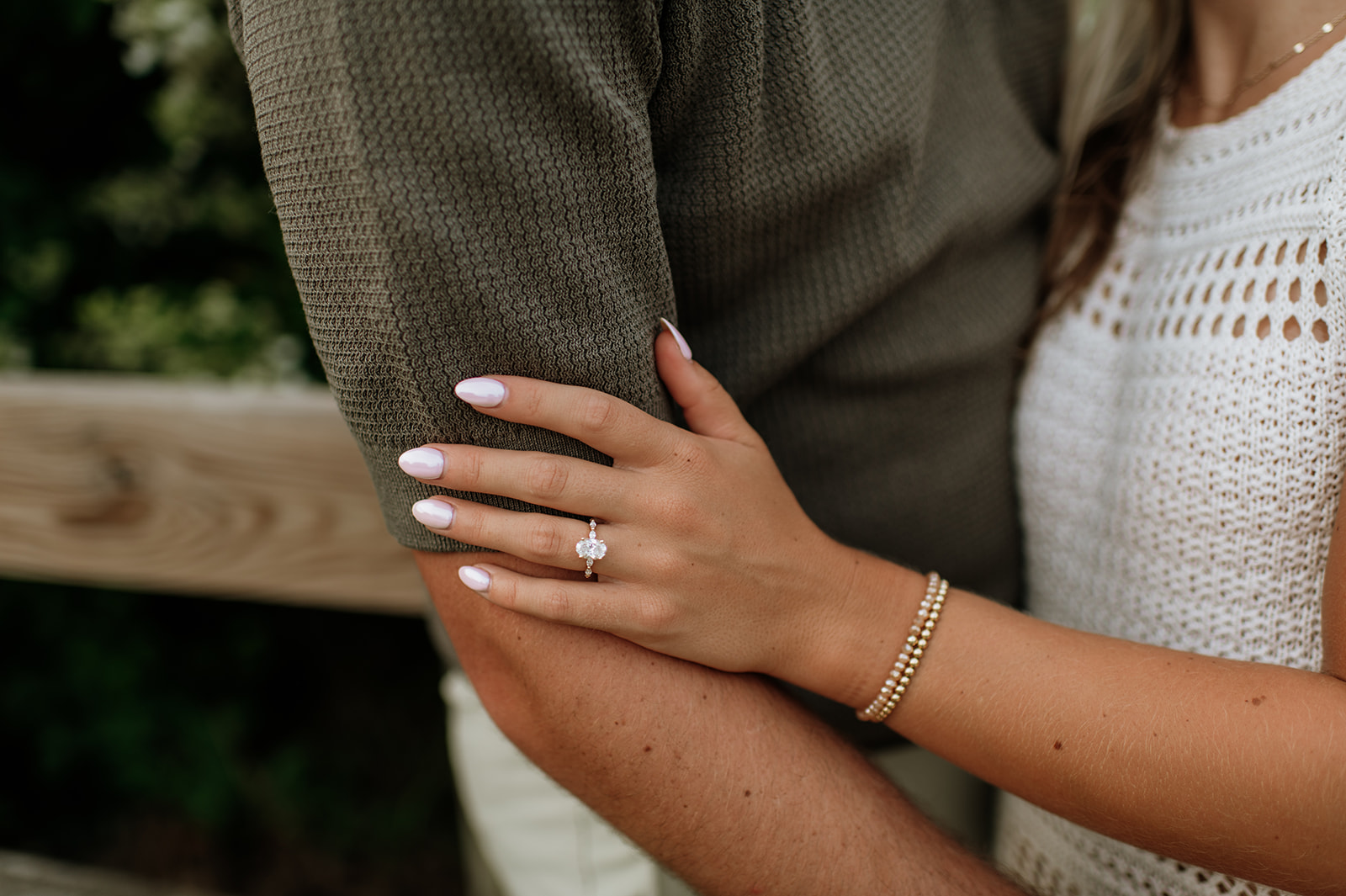 Close up shot of a woman holding her fiancés arm while showing her engagement ring.