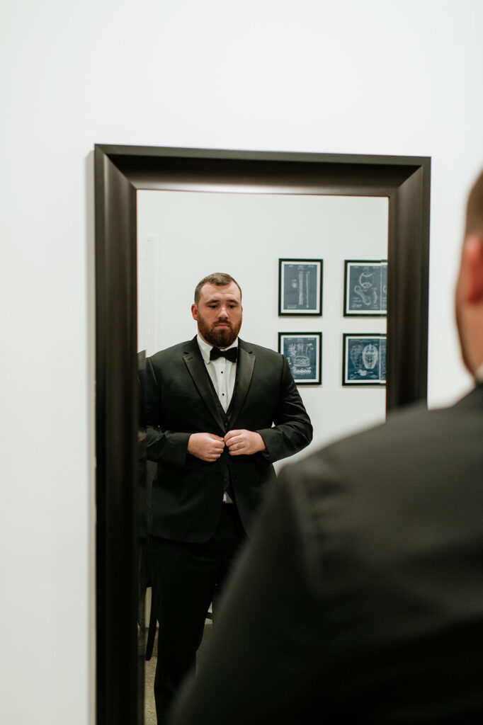 The groom looking at himself in a full length mirror as he gets ready in the Grooms Lounge.