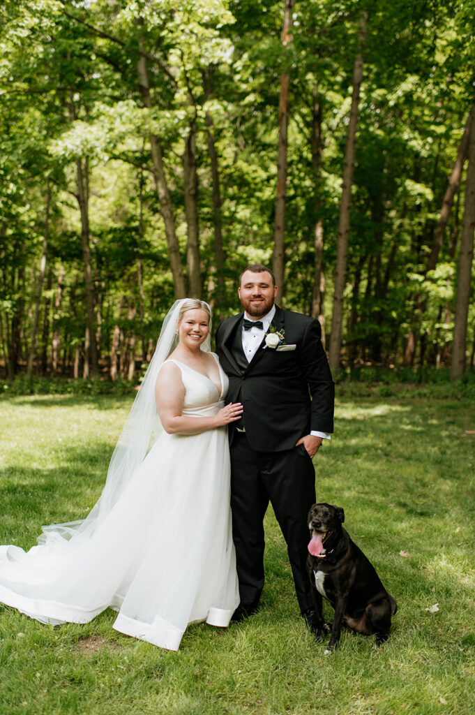 Bride and groom posing with their dog on the open lawn area.